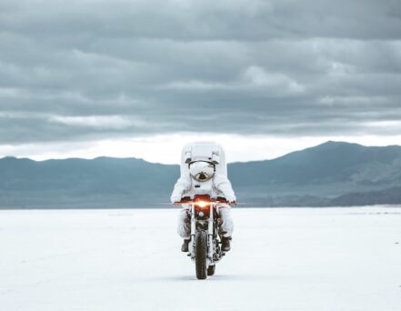 person riding a motorcycle in a space suit on salt flats